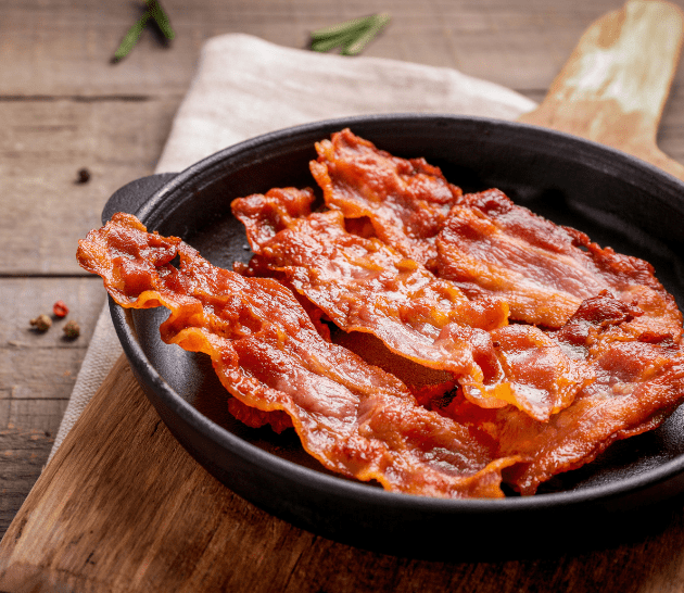 Bacon croustillant posé dans une poêle en fonte placée sur une planche à découper en bois